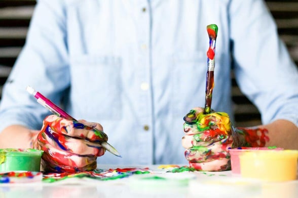 person holding painbrushes while his hands are covered in paint, signifying an art teacher