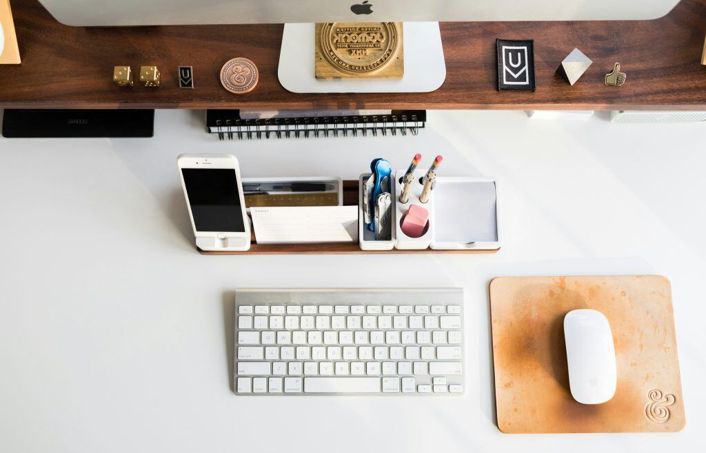 Organized desk with a keyboard, mouse, smartphone, pens, and office supplies arranged neatly in front of a computer monitor.