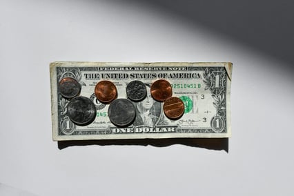A one-dollar bill with several U.S. coins, including pennies, nickels, dimes, and quarters, placed on top.