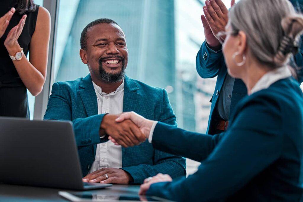 Smiling black man in a suit shaking hands with coworker, signifying a 'welcome to the team' moment